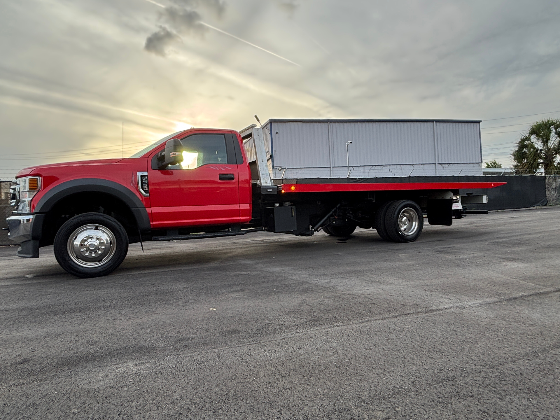 Red flatbed transporting a service load at sunset